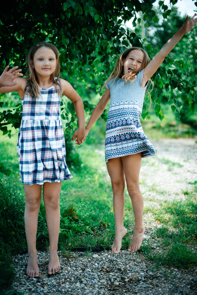 Two girls in the fresh air are jumping for joy. Girls posing, nature on the background. The concept of sports and positive. Outdoor activities.  Copy space. Toning.  - Foto, Imagen