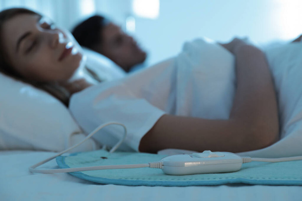Couple sleeping in bed with electric heating pad, focus on cable - Foto, imagen
