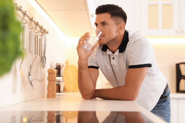 Man drinking glass of pure water at countertop in kitchen - Фото, изображение