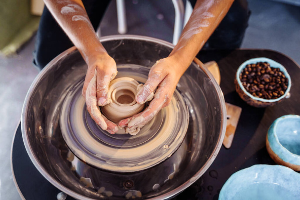 Close-up van de handen van een vrouwelijke keramist werkend met een pottenbakkerswiel in een gezellige, lichte werkplaats. Een jonge, ervaren vrouw maakt vakkundig een mok, vaas of bord. Creatieve mensen, aardewerk workshop. - Foto, afbeelding