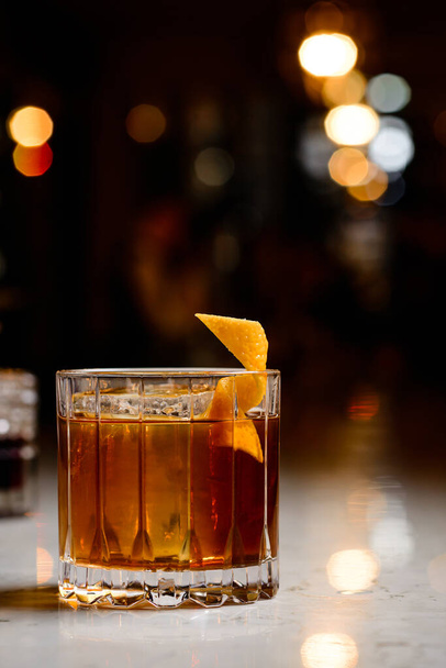 Closeup classic godfather cocktail with slice of orange and ice cubes at bright bar background. Alcoholic cocktail Godfather with orange peel and ice - Valokuva, kuva