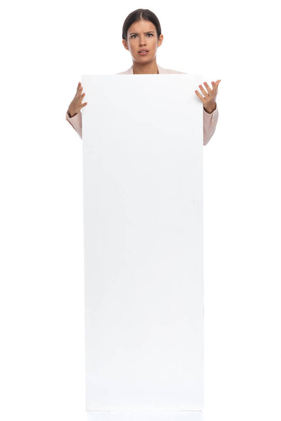 zdezorientowana bizneswoman w różowej kurtce pokrywającej korpus z pustą deską, stojąca na białym tle w studio - Zdjęcie, obraz