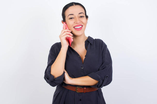 Portrait of a smiling Arab woman wearing dress against white studio background  talking on mobile phone. Business, confidence and communication concept. - Foto, Bild