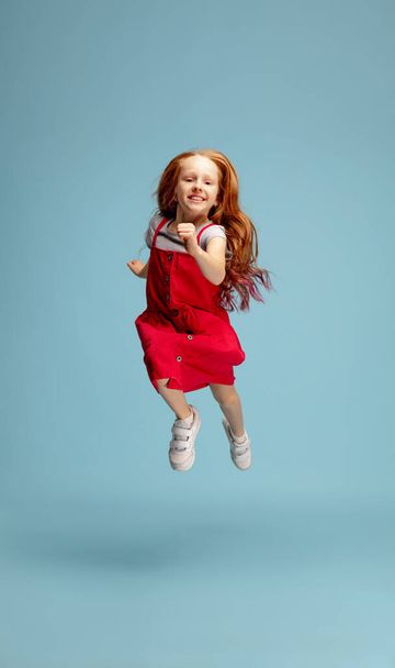 Happy redhair girl isolated on blue studio background. Looks happy, cheerful, sincere. Copyspace. Childhood, education, emotions concept - Photo, image