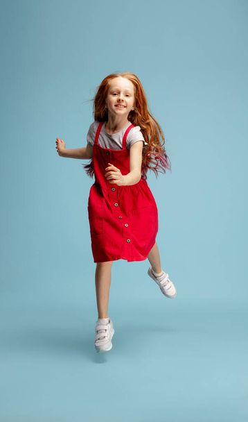 Happy redhair girl isolated on blue studio background. Looks happy, cheerful, sincere. Copyspace. Childhood, education, emotions concept - Фото, зображення