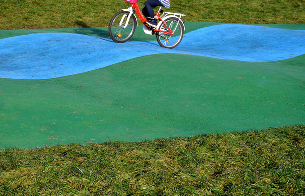 Παιδική παιδική χαρά στο πάρκο. χρωματιστό ελαστικό tartan προστατεύει τα παιδιά όταν πέφτουν από το ποδήλατο. την ικανότητα επαλήθευσης με μαχαίρι σε στροφές και κυματιστές διόδους της τροχιάς. - Φωτογραφία, εικόνα