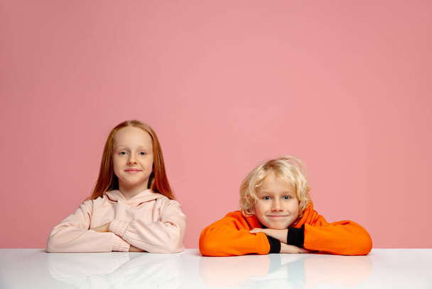 Happy children isolated on coral pink studio background. Look happy, cheerful, sincere. Copyspace. Childhood, education, emotions concept - Фото, изображение