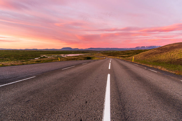 Prachtige zomer zonsondergang over een kronkelende bergweg die naar beneden leidt naar een vallei. Bergen zijn zichtbaar aan de horizon. Myvatn, IJsland. - Foto, afbeelding