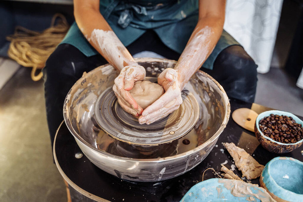 With professional hand movements, a female potter prepares a piece of clay on a potter's wheel, kneads the clay and rolls it out to make a bowl, vase, jug, plate. Pottery studio. Young professional. - Photo, Image