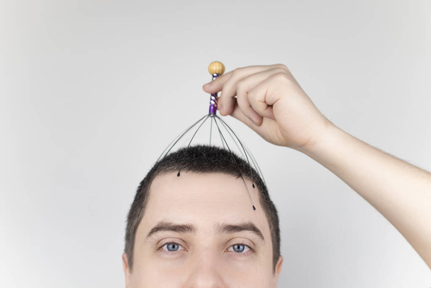 Muž na bílém pozadí si udělá masáž hlavy kapilárním masérem. Samostatná pomoc, antistresová a relaxační koncepce - Fotografie, Obrázek