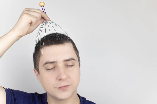 Un uomo su uno sfondo bianco si fa un massaggio alla testa con un massaggiatore capillare. Concetto di auto-aiuto, anti-stress e relax - Foto, immagini