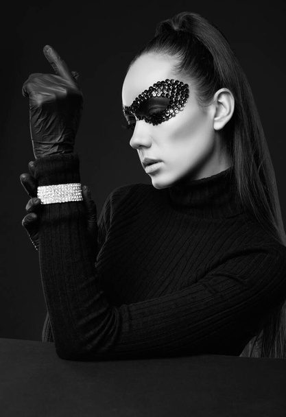 Portret uroczej eleganckiej brunetki w swetrze z golfem i cekinami maska pozowanie na czarnym tle w studio - Zdjęcie, obraz