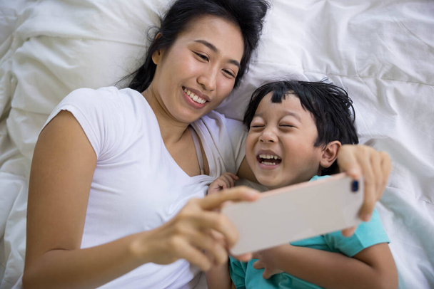close up of happy mother and her son Taking pictures or selfie or video call or relatives in a bed. Concept of new generation, family, parenthood, authenticity, connection - Foto, afbeelding