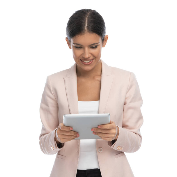 enthusiastische Geschäftsfrau in pinkfarbener Jacke, mit Tab und Nachrichten lesen, lächelnd und isoliert posierend auf weißem Hintergrund im Studio - Foto, Bild