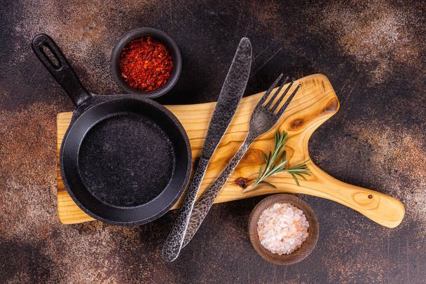 Empty black round  iron pan with handle on  wooden cutting board. Cooking background concept.  - Photo, image