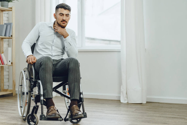 Young disabled man sitting in a wheelchair near the window - Φωτογραφία, εικόνα