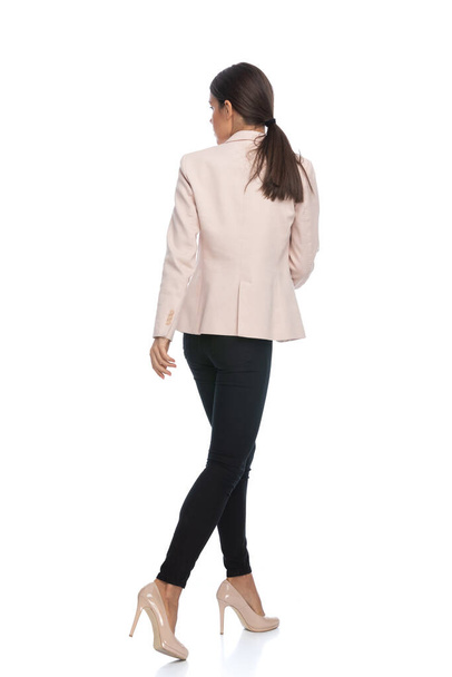 back view of young businesswoman in pink jacket looking to side and walking isolated on white background in studio, full body - Fotó, kép