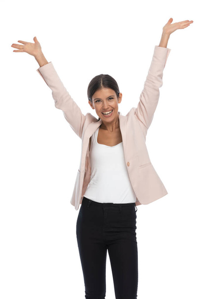 mujer casual inteligente emocionada en chaqueta rosa sosteniendo los brazos en el aire, animando y riendo sobre fondo blanco en el estudio - Foto, imagen