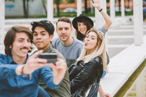 Grupo de amigos multiétnicos al aire libre divertirse y tomar selfie utilizando el teléfono inteligente al aire libre en la ciudad  - Foto, Imagen