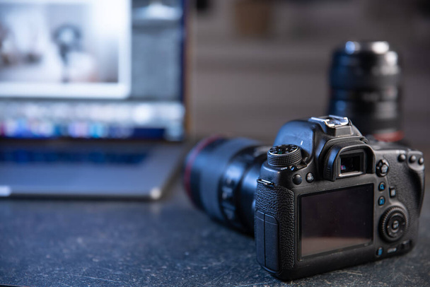 Câmera profissional em um fundo embaçado com um laptop. O conceito de trabalhar com fotos e vídeos. - Foto, Imagem