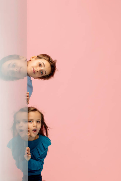 Happy children isolated on coral pink studio background. Look happy, cheerful, sincere. Copyspace. Childhood, education, emotions concept - Фото, изображение