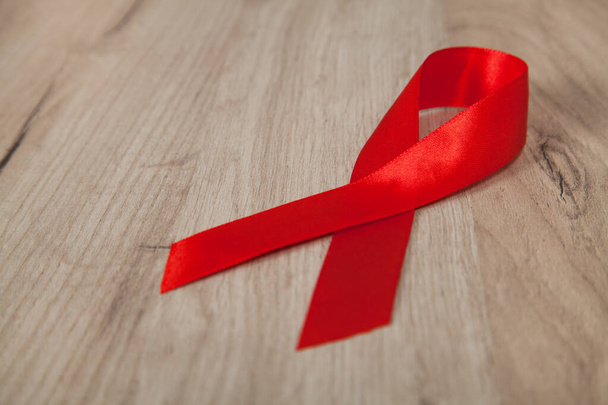 Κόκκινη κορδέλα - σύμβολο ευαισθητοποίησης και υποστήριξης για όσους ζουν με HIV, ξύλινο υπόβαθρο. - Φωτογραφία, εικόνα