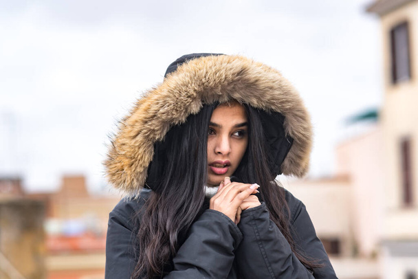 Cute young woman freezing in winter coat standing in street - Photo, Image