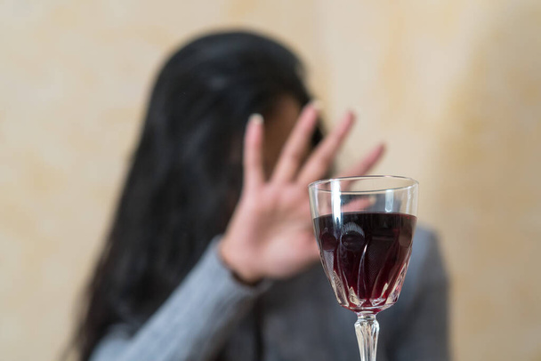Giving up alcohol. A young woman at the table refuses a glass of red wine with her hand - Foto, Bild