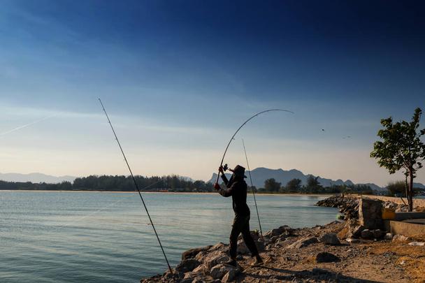 漁師は、タイのPhetchaburi県Cha-Amの青い空と晴れた日に海にスイングと釣りフライロッドをスローします。レジャー・スポーツ活動. - 写真・画像