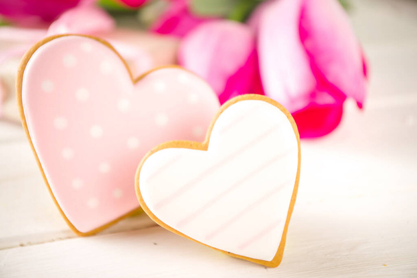 バレンタインデーのコンセプト、春の女性の休日、母の日の背景、赤いチューリップの花花束、クラフト紙のギフトボックス、ハート型の伝統的な砂糖クッキー、白い木製の背景コピースペース - 写真・画像