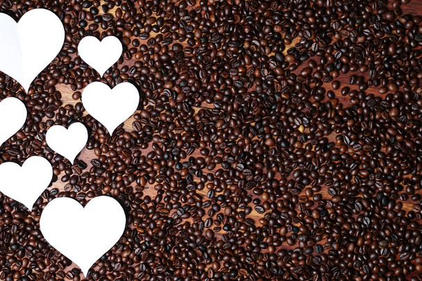 Papierowe paski w kształcie serca na tle ziarna kawy. Połączenie ziaren kawy i symbolu miłości z okazji Światowego Dnia Miłości lub tak zwanych Walentynek. Walentynki z ziarnem kawy. - Zdjęcie, obraz