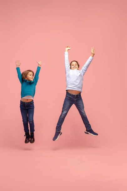 Happy children isolated on coral pink studio background. Look happy, cheerful, sincere. Copyspace. Childhood, education, emotions concept - Foto, Imagen
