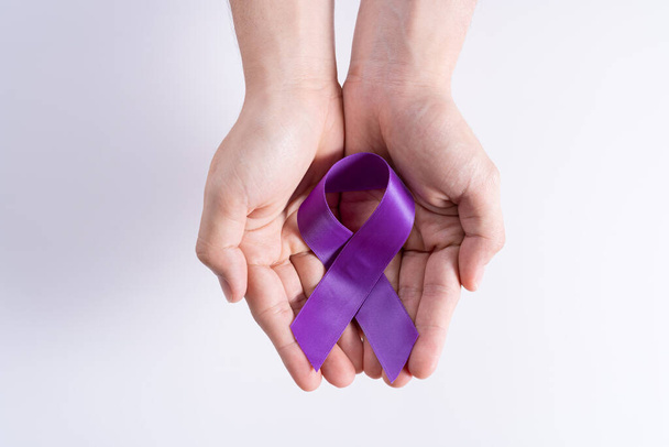 Día Mundial del Cáncer, manos sosteniendo cinta púrpura sobre fondo gris con espacio de copia para texto. Salud y concepto médico. - Foto, Imagen