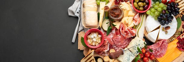 Appetizers table. Cheese, fuits and meat board on dark  background. Top view, copy space, panorama - Foto, Bild
