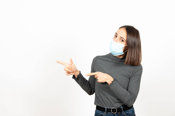 Hispanische Frau zeigt auf den Kopierraum und schaut in die Kamera, während sie eine medizinische Gesichtsmaske trägt. Gesundheitsversorgung während der Coronavirus-Pandemie. - Foto, Bild