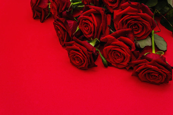 マットな赤いファミランの背景に新鮮なバーガンディのバラの花束。香りの赤い花、バレンタインデー、結婚式や誕生日のためのギフトコンセプト、コピースペース - 写真・画像