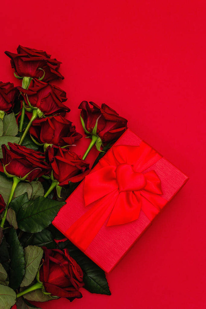 Bouquet of fresh burgundy roses and gift box on a matte red foamiran background. Fragrant red flowers, gift concept for Valentine's Day, Wedding or Birthday, top view - Photo, Image