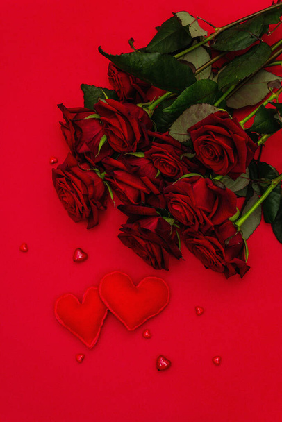 Kytice čerstvě vínových růží a měkkých plstěných srdcí na matně červeném pěnovém pozadí. Vůně červené květy, koncept dárku na Valentýna, svatba nebo narozeniny, byt ležel - Fotografie, Obrázek