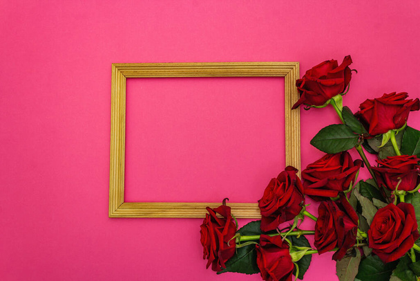 Valentine Day or Wedding concept with fresh burgundy roses and wooden frame. Matte pink background, flat lay - Photo, Image