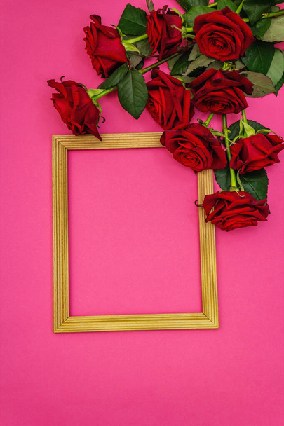 Valentine Day or Wedding concept with fresh burgundy roses and wooden frame. Matte pink background, flat lay - Photo, Image