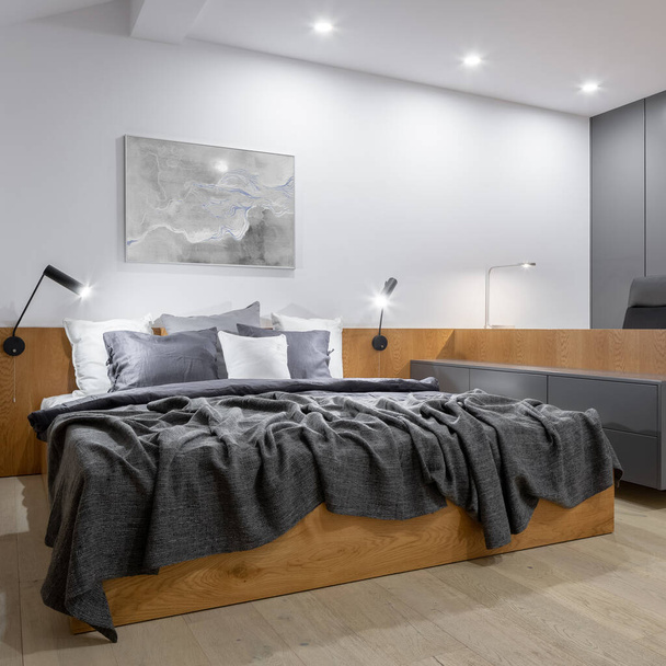 Stylish and modern bedroom with comfortable bed with wooden frame, long wooden desk and wooden floor - 写真・画像