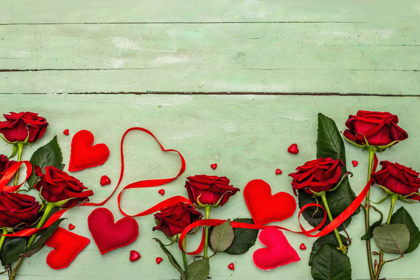 День святого Валентина оточений рясними серцями, свіжими бургундськими трояндами і червоною святковою стрічкою. Дерев "яний ніжний зелений фон, плоский вид. - Фото, зображення