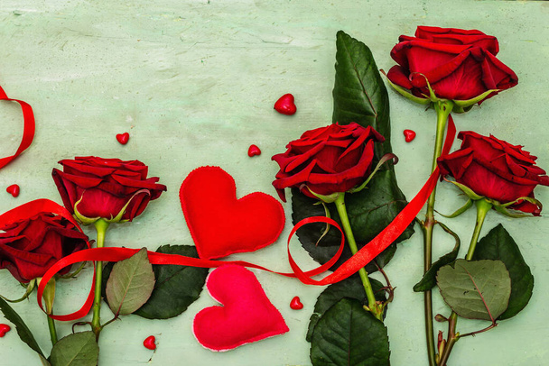 Valentýn pozadí s pestrým srdcem, čerstvé burgundské růže a červenou slavnostní stuhou. Staré dřevěné jemné zelené pozadí, byt ležel, horní pohled - Fotografie, Obrázek