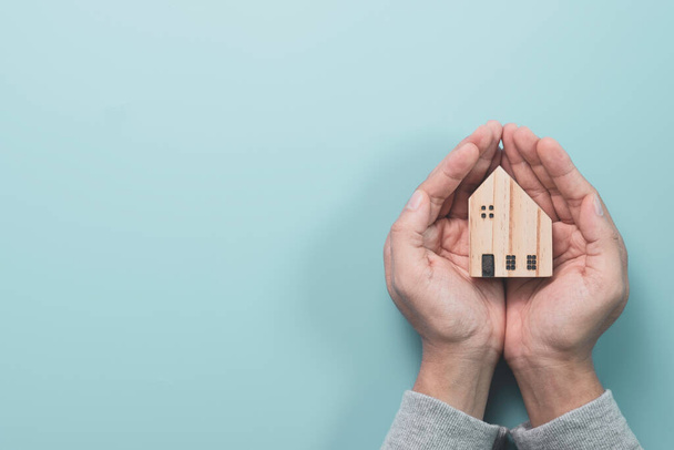 Επιχειρηματίας κρατώντας ξύλινο σπίτι μοντέλο σε μπλε φόντο, Προστατέψτε το σπίτι και το περιουσιακό στοιχείο έννοια. - Φωτογραφία, εικόνα