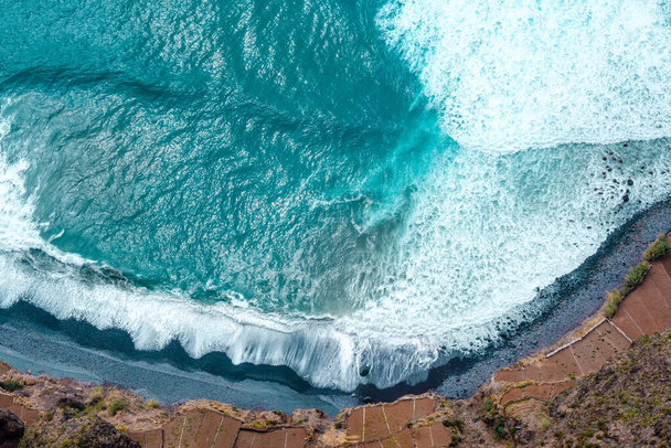 Punto di vista aerea del mare schiantarsi onde sulla spiaggia di pietra nera con campi coltivati accanto ad esso. - Foto, immagini