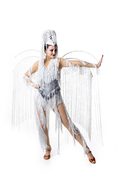 Beautiful young woman in carnival, stylish masquerade costume with feathers dancing on white studio background. Concept of holidays celebration, festive time, fashion - Foto, imagen