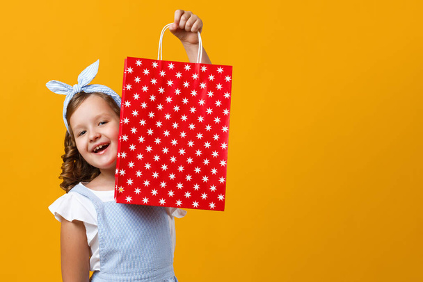 Fröhliches Mädchen in der Hand einer Papiertüte mit dem Kauf. Nettes Kind auf gelbem Hintergrund. - Foto, Bild