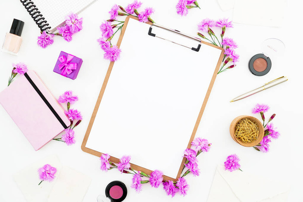 Espacio para tareas femeninas con portapapeles, cuaderno, flores rosadas y accesorios sobre fondo blanco. Piso tendido, vista superior. - Foto, imagen
