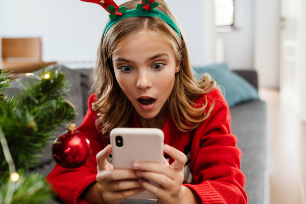 Shocked caucasian girl wearing toy deer horns using cellphone at home - Photo, image
