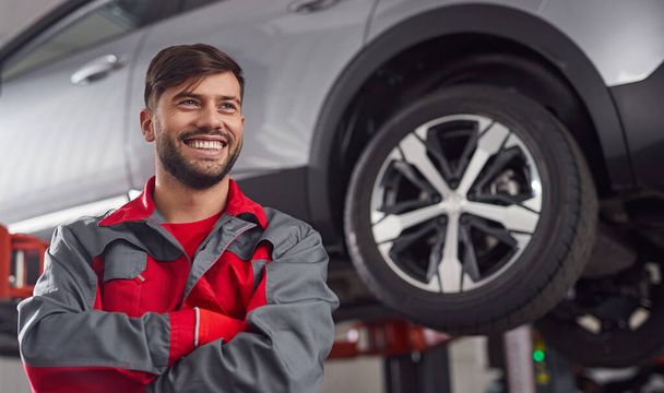 Cheerful mechanic standing near car in workshop - Zdjęcie, obraz